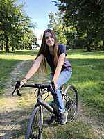 Die Schülerin Elisabeth Mardicke steht, auf einem schwarzen Rennrad sitzend, auf einem Waldweg im Grünen und lächelt in die Kamera – Freizeit, Natur und Fahrradfahren im Park.
